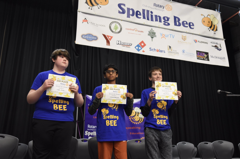 Three students hold certificates after participating in a Spelling Bee.